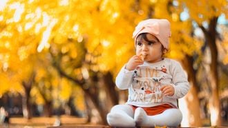 Peuter die buiten in de herfst zit en voedsel eet waarin ze kan stikken