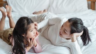 Moeder die met haar kind op bed ligt en praat over heftige nieuwsberichten