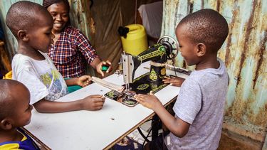 opvoedgewoontes / Keniaans gezin zit om naaimachine heen