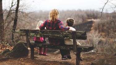 moeder en kinderen zitten op een bankje in de rustige natuur