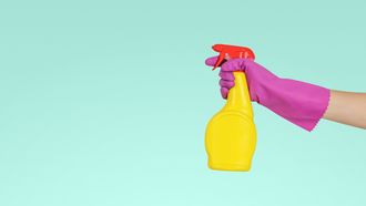 Hand met paarse schoonmaakhandschoen en schoonmaakmiddel, klaar voor het schoonmaken