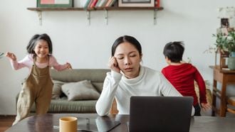 geduld / moeder aan tafel met laptop met kinderen op achtergrond