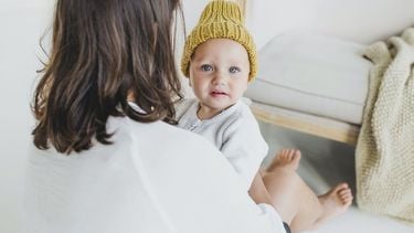 Moeder die een baby vasthoudt die een gele muts op heeft en een Hollandse jongensnaam heeft gekregen