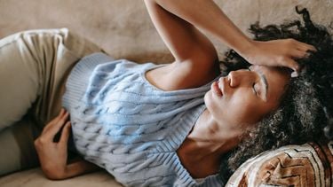 Vrouw ligt met buikpijn op de bank en is waarschijnlijk te vroeg ongesteld