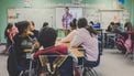 Kinderen in de klas met een meester bij het bord die goed begeleid bij het van school veranderen van een van de kinderen
