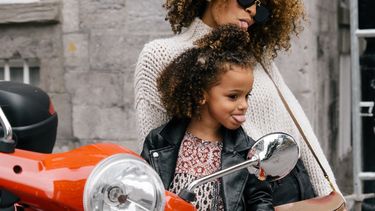 Jonge moeder met haar dochter op een scooter die een tong uitsteken naar de spiegel