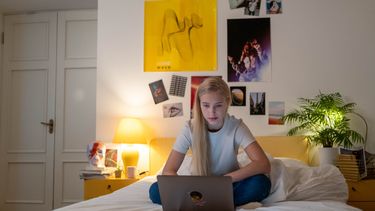 Tiener op bed met laptop ervaart stress