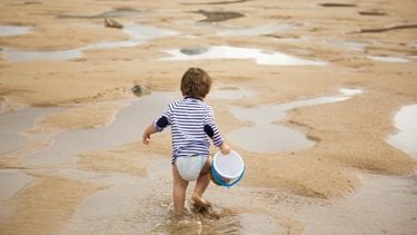 Peuter loopt op het strand om een emmertje water te halen