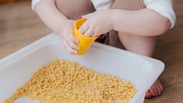 Kind dat sensopathisch aan het spelen is met macaroni